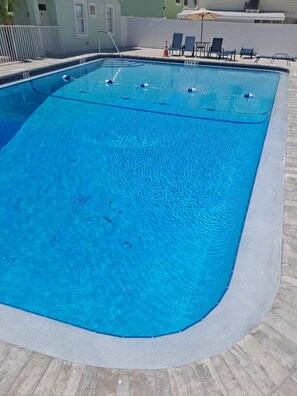 A rectangular swimming pool with clear blue water, surrounded by a stone deck and a white wall. - Beachside 1-bedroom condo with swimming pool (Redington Shores)