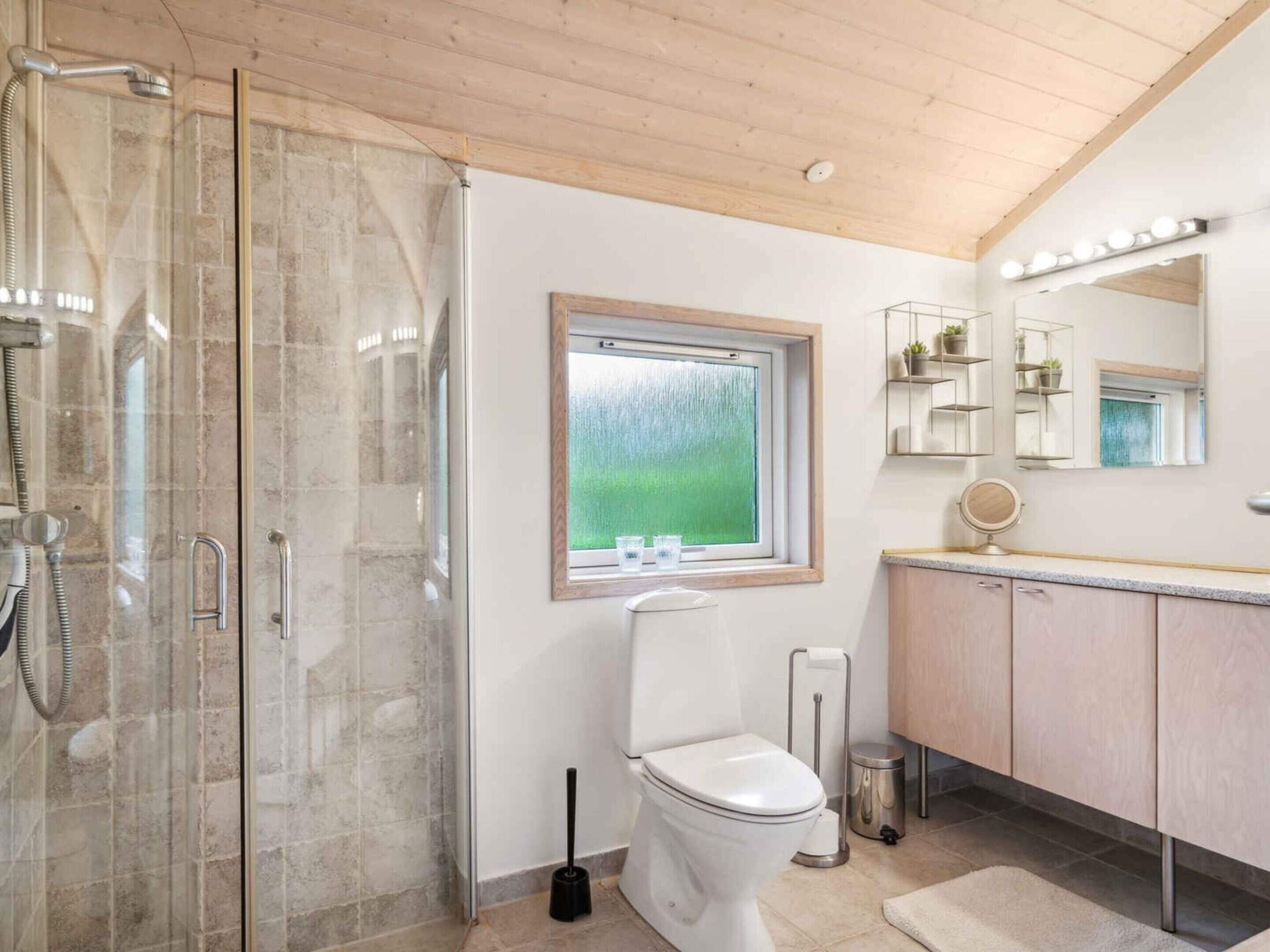 Een badkamer met een douchecabine van glas, een toilet, een bidet, een raam met uitzicht en een wastafel met spiegel en verlichting.