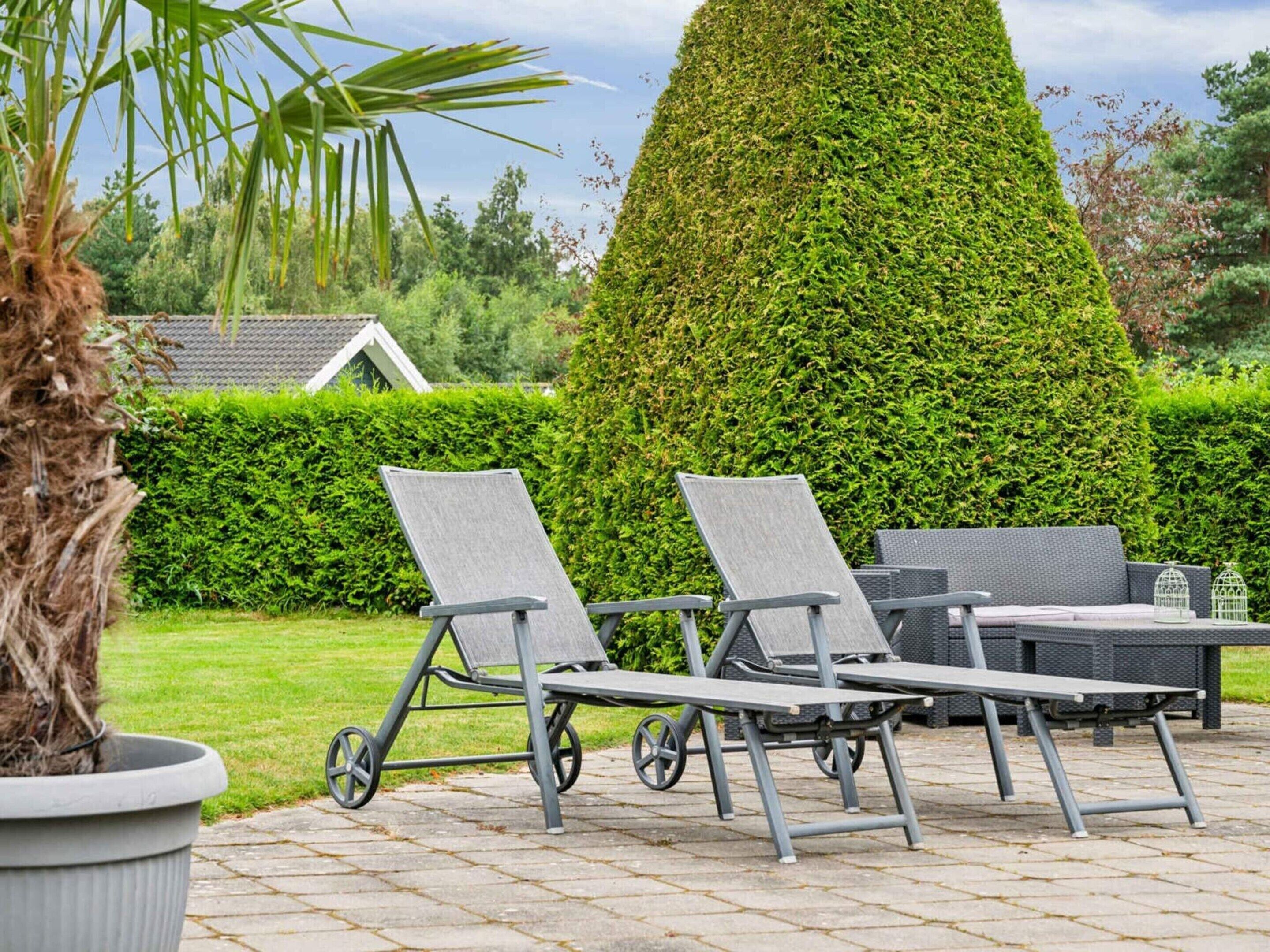 A patio with a neatly trimmed hedge, outdoor furniture, and a potted plant.