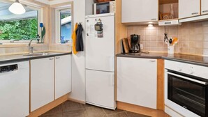 Eine moderne Küche mit weißen Schränken, einem Kühlschrank, einer Kaffeemaschine und einem Fenster mit Blick auf Grünflächen.