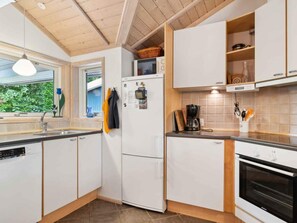 Eine moderne Küche mit weißen Schränken, einem Kühlschrank, einer Kaffeemaschine und einem Fenster mit Blick auf Grünflächen.