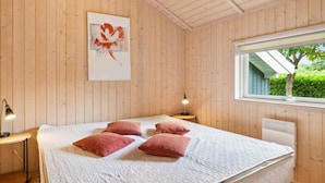 Ein Zimmer mit Holzwandverkleidung, einem Bett, einem Fenster und einem an der Wand hängenden Kunstwerk.