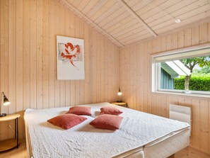 Ein Zimmer mit Holzwandverkleidung, einem Bett, einem Fenster und einem an der Wand hängenden Kunstwerk.