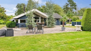 Ein Haus mit überdachter Terrasse, Gartenmöbeln und einem gepflegten Rasen.