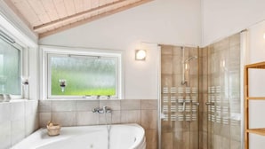 Ein Badezimmer mit einer freistehenden Badewanne, einer gläsernen Duschkabine und einem Fenster mit Blick auf Grünflächen.