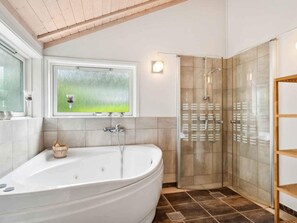 Ein Badezimmer mit einer freistehenden Badewanne, einer gläsernen Duschkabine und einem Fenster mit Blick auf Grünflächen.