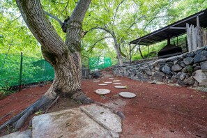 Un chemin de pierres menant à une zone abritée, avec un mur en pierre et un arbre.