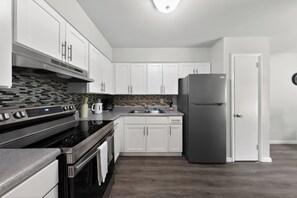 A modern kitchen with white cabinets, a stainless steel refrigerator, and a black stove. - Elegant Chateau Escape | Parking Included (Wilmington)