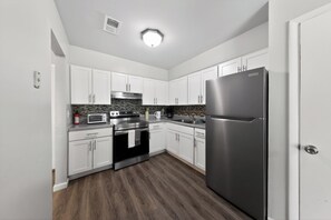 A modern kitchen with white cabinets, stainless steel appliances, and a wooden floor. - Elegant Chateau Escape | Parking Included (Wilmington)