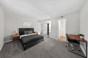 A bedroom with a bed, bedside tables, a desk, and a chair. There is a door leading to another room. - Elegant Chateau Escape | Parking Included (Wilmington)