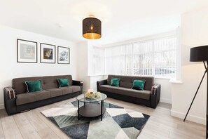 A modern living room with two sofas, a coffee table, and a large window. - Birmingham Estate | Ultimate Summer Getaway (Winson Green)
