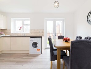 A modern kitchen with a built-in washing machine, a dining area with a table and chairs, and a large wall clock. - Birmingham Estate | Ultimate Summer Getaway (Winson Green)