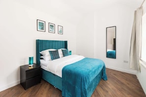 A bedroom with a teal bed, white bedding, a black nightstand, and a mirror on the wall. - The Newhall Loft | Spacious Private Duplex in JQ (West Midlands)