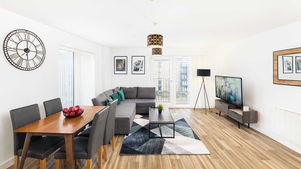Ein modernes Wohnzimmer mit Sofa, Esstisch, Stühlen, Couchtisch, einer Uhr, Kunstwerken, einem Fernseher und einer Lampe.