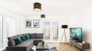 Ein modernes Wohnzimmer mit einem Ecksofa, einem Couchtisch, einem Fernseher und einer Stehlampe.