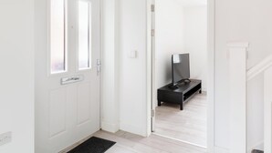 A hallway with a white door, a black bench, and a television on a stand. - Birmingham Estate | Made For Group Memories (Birmingham)
