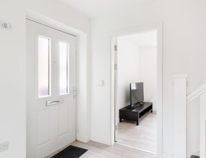 A hallway with a white door, a black bench, and a television on a stand. - Birmingham Estate | Made For Group Memories (Birmingham)