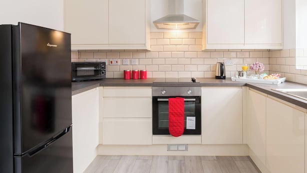 A modern kitchen with a black refrigerator, a microwave, a stove, and a red oven mitt hanging on the oven handle. - Birmingham Estate | Made For Group Memories (Birmingham)