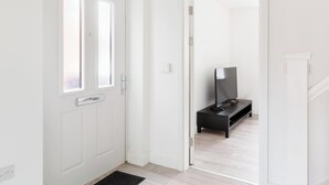 Un pasillo con una puerta blanca, un banco negro y un televisor sobre un mueble.