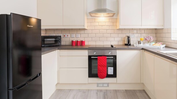 Una cocina moderna con un refrigerador negro, un microondas, una estufa y un guante rojo colgado del pomo del horno.