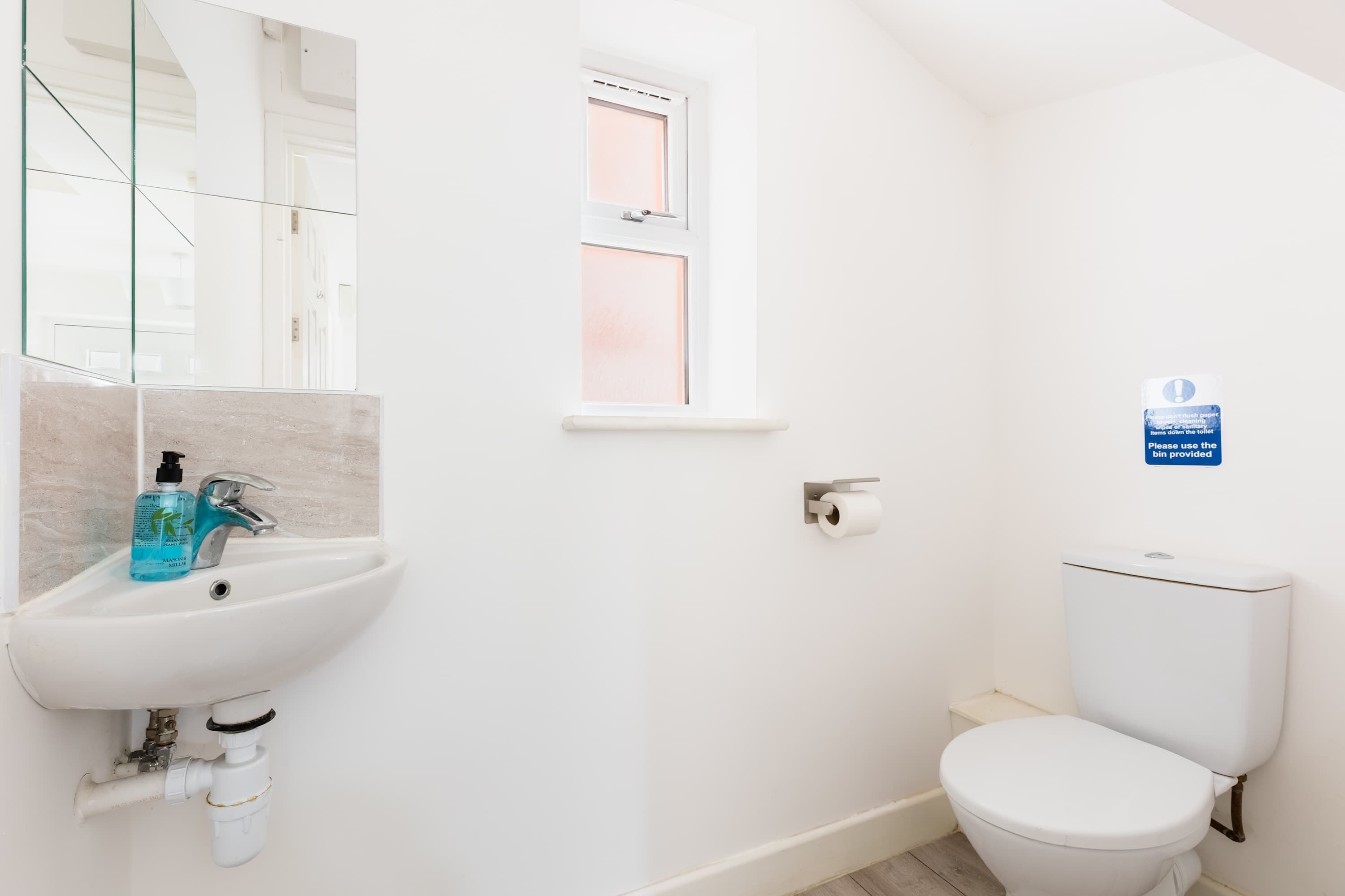 Un baño con lavamanos blanco, un espejo, una ventana y un inodoro.