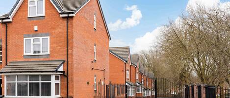 A row of red brick houses with black metal gates, a clear sky, and leafless trees.