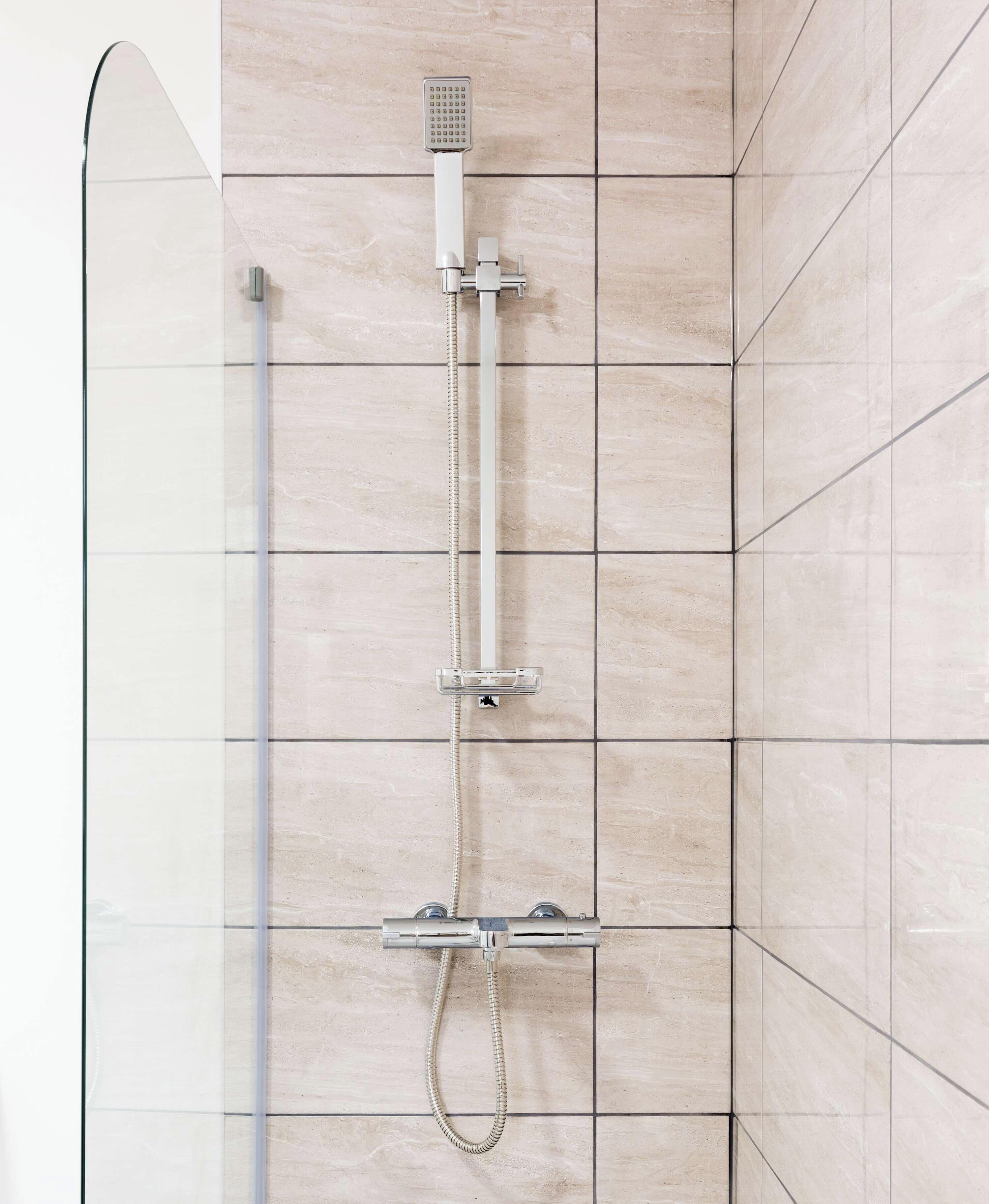 A shower with a handheld showerhead and a fixed showerhead, both mounted on a wall with a tiled surface.
