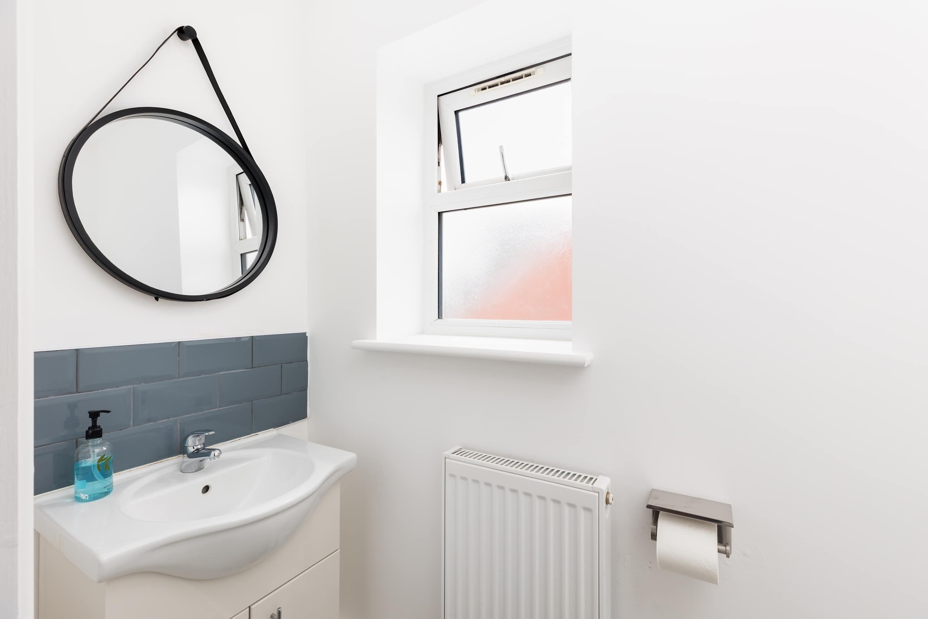 A bathroom with a white sink, a mirror, a window, and a toilet paper holder.