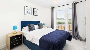 A bedroom with a bed, nightstands, a window with curtains, and framed pictures on the wall. - St Lukes Retreat | Modern Top Floor City Escape (West Midlands)