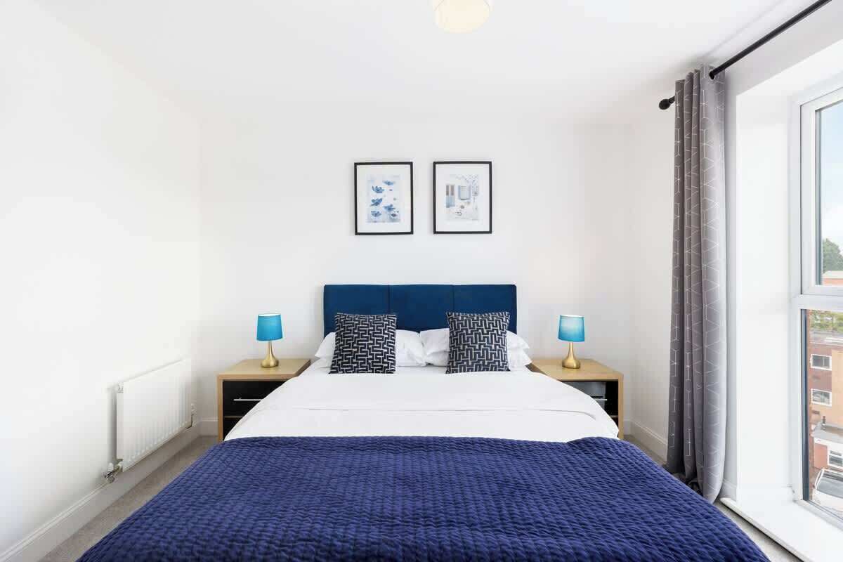 Une chambre d’hôtel avec un lit, deux tables de chevet, une fenêtre et deux tableaux encadrés au mur.