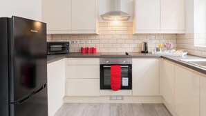 A modern kitchen with a black refrigerator, a microwave, a stove, and a red oven mitt hanging on the oven handle. - Birmingham Estate | Gather Stay & Celebrate (Winson Green)
