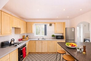 A modern kitchen with wooden cabinets, a gas stove, a microwave, and a sink. - Anchor House | Spacious Group Stay | Free Parking (West Midlands)