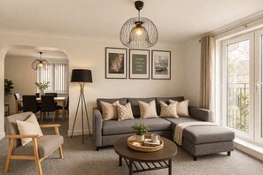 A living room with a grey sofa, a coffee table, a floor lamp, and framed pictures on the wall. - Anchor House | Spacious Group Stay | Free Parking (West Midlands)