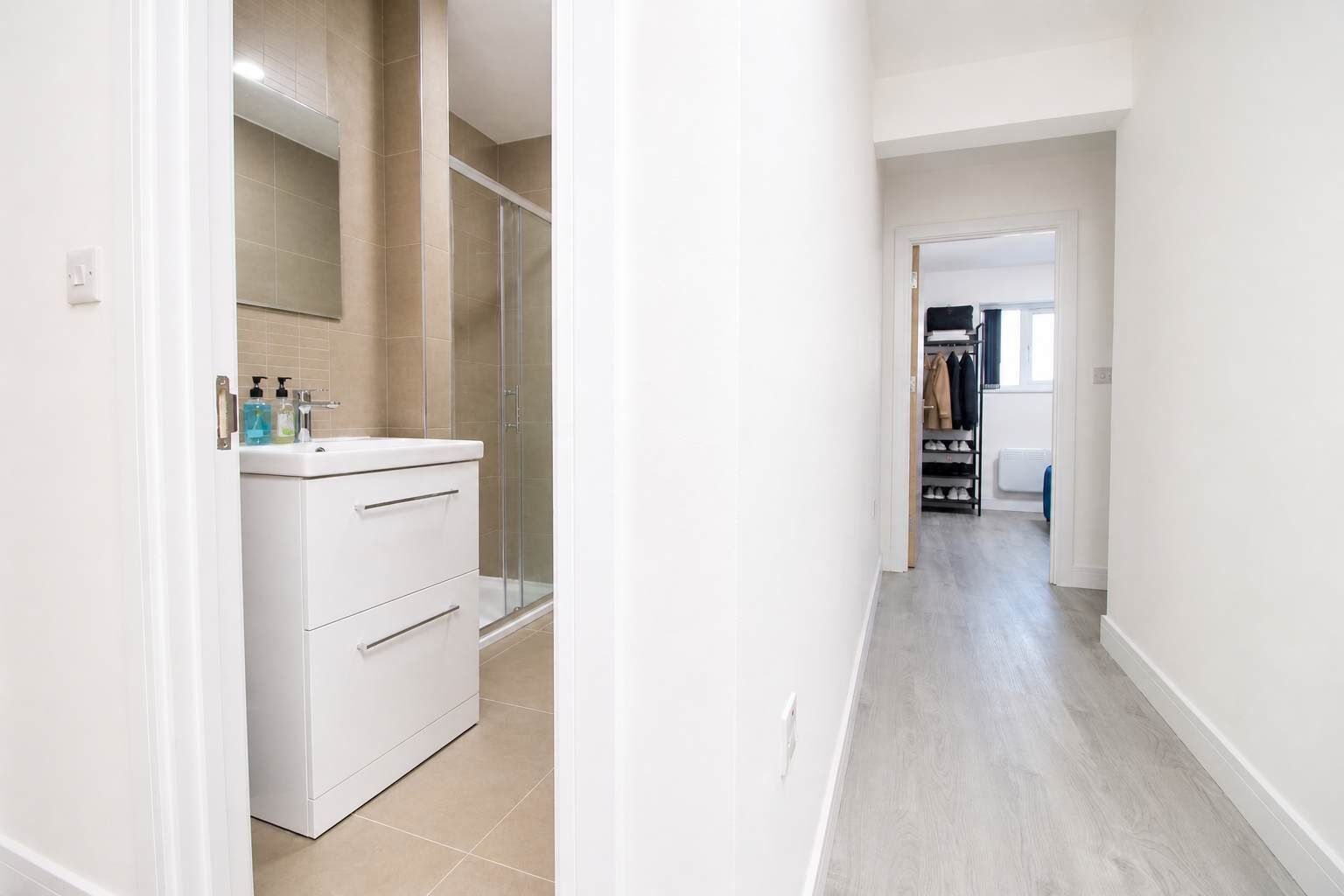 A hallway with a white vanity, a glass shower enclosure, and a shoe rack.