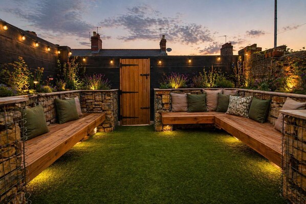 A cozy outdoor seating area with stone walls, a wooden bench, and string lights.