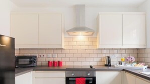 Une cuisine moderne avec des armoires blanches, un micro-ondes noir, une hotte de cuisinière en acier inoxydable et un dosseret en briques.