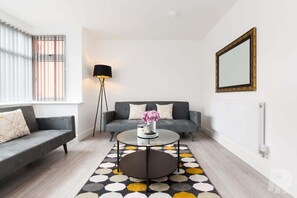 A modern living room with a sofa, a coffee table, a floor lamp, and a patterned rug. - Birmingham Estate | Private Gated Group Escape (Winson Green)