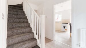 Un escalier avec une rampe blanche menant à une cuisine équipée d’un lave-linge.