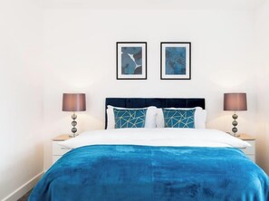 A hotel room with a bed, two framed artworks, a nightstand with a lamp, and a bedside table. - Birmingham Estate | Private Gated Group Escape (Winson Green)