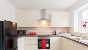 A modern kitchen with a black refrigerator, a microwave, a stove, and a red oven mitt hanging on the oven handle. - Birmingham Estate | Gated | Built For Large Groups (Winson Green)
