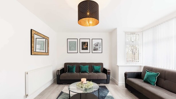 A modern living room with a sofa, a coffee table, and framed pictures on the wall. - Birmingham Estate | Gated | Built For Large Groups (Winson Green)