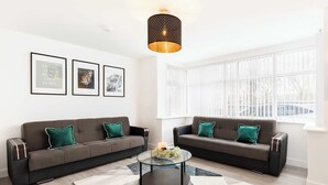 A modern living room with two sofas, a coffee table, and framed pictures on the wall. - Birmingham Estate | Gated | Built For Large Groups (Winson Green)