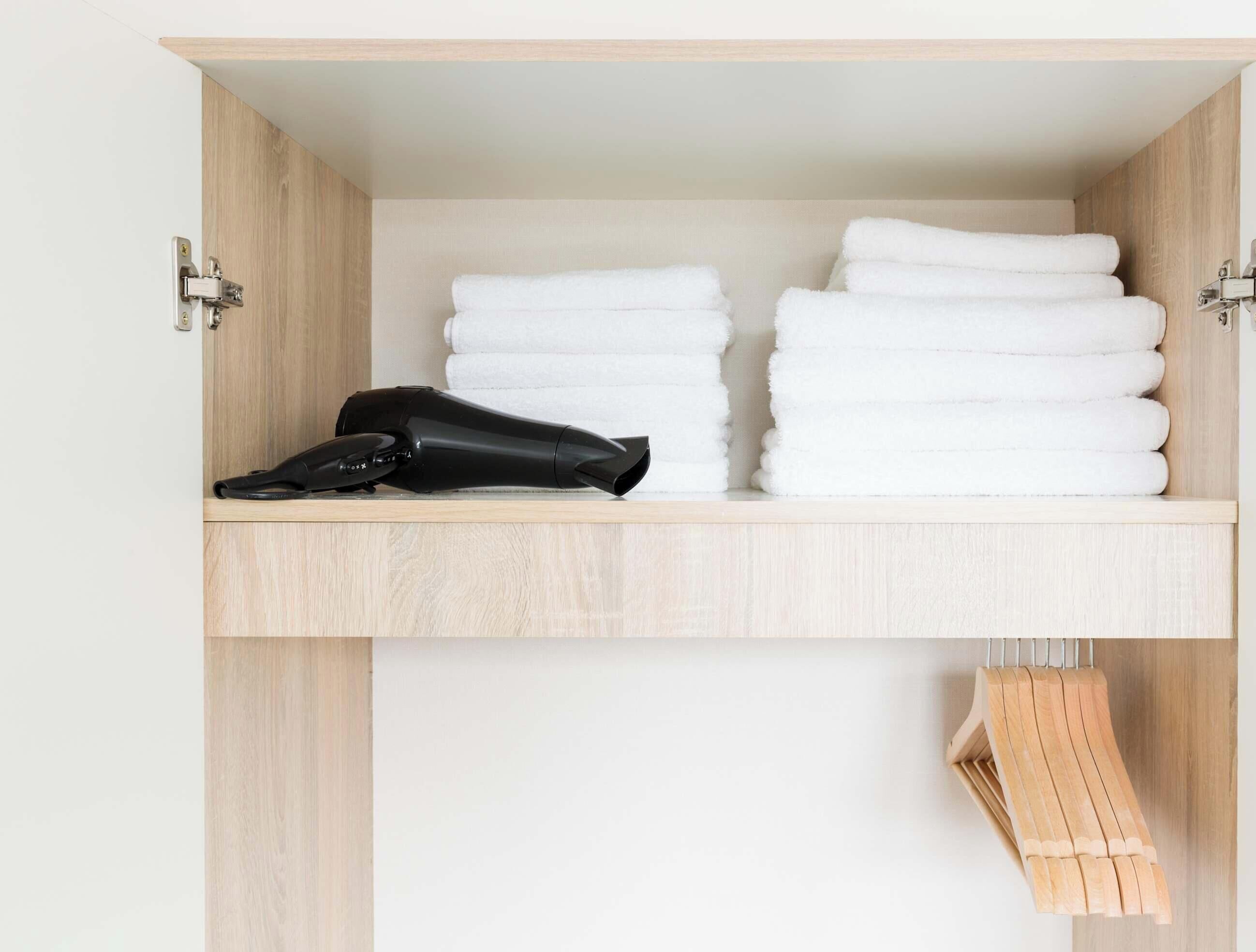 A closet with neatly folded white towels and a black hairdryer on a shelf.