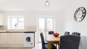A modern kitchen with a built-in washing machine, a dining area with a table and chairs, and a large wall clock. - Birmingham Estate | Gated | Built For Large Groups (Winson Green)