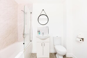 A bathroom with a glass-enclosed shower, a white sink with a mirror above it, and a toilet. - Birmingham Estate | Gated | Built For Large Groups (Winson Green)