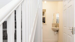A narrow hallway leading to a bathroom with a sink and mirror. - Birmingham Estate | Gated | Built For Large Groups (Winson Green)