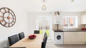Een moderne keuken met een wasmachine, een eettafel met stoelen en een grote wandklok.