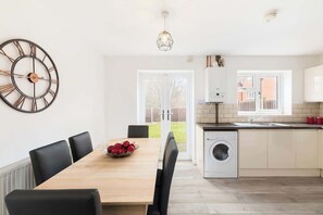 A modern kitchen with a washing machine, a dining table with chairs, and a large wall clock. - Birmingham Estate | Detached Home for Togetherness (Birmingham)