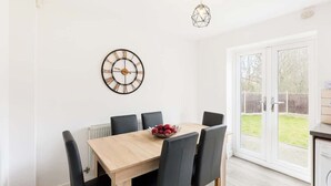 Een eetruimte met een houten tafel, zwarte stoelen, een fruitschaal, een wandklok en een hangende lamp.