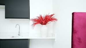 Une salle de bain moderne avec un lavabo blanc, un robinet chromé, un vase blanc contenant des fleurs rouges et un meuble sombre.